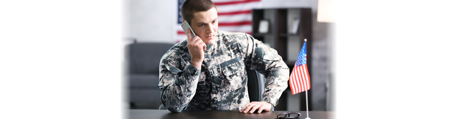 Soldier talking by mobile phone while sitting at table in headquarters building